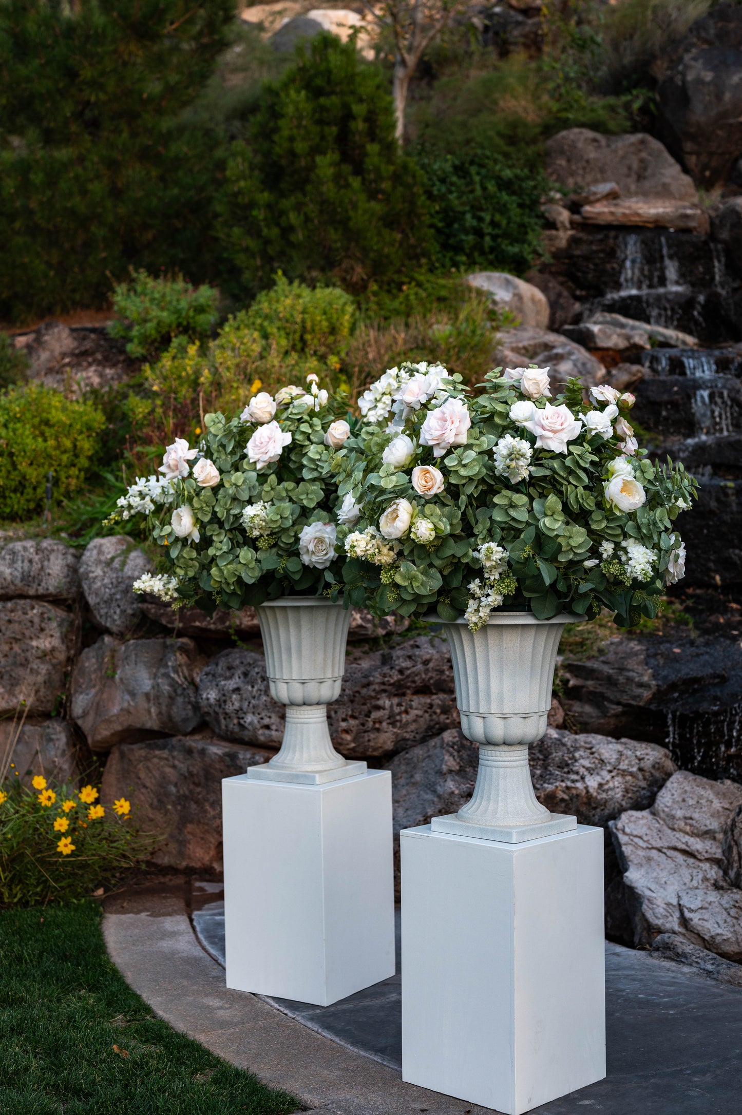 Two wedding urns filled with flowers placed on pedestals for wedding rentals